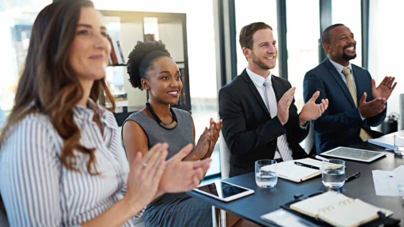 Imagem de um grupo de pessoa no que parece ser uma sala de reuniões apaludindo e sorrindo