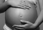 Imagem em preto e branco de uma grávida com as mãos na barriga