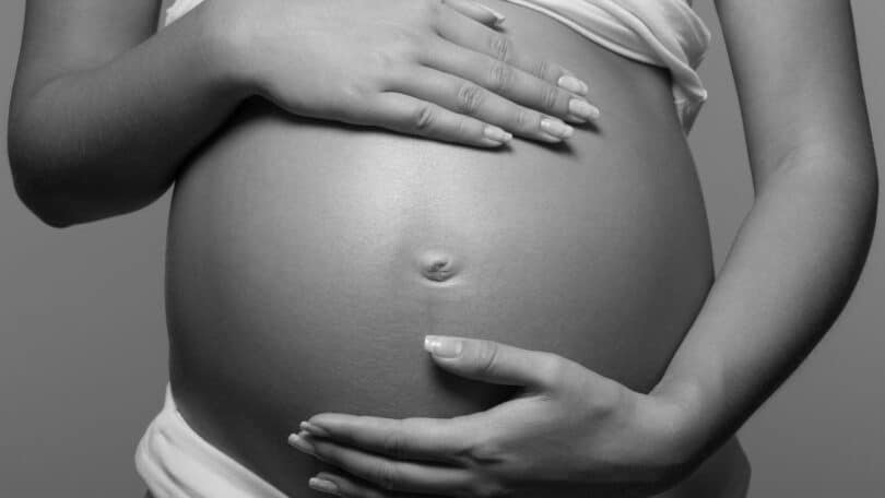 Imagem em preto e branco de uma grávida com as mãos na barriga