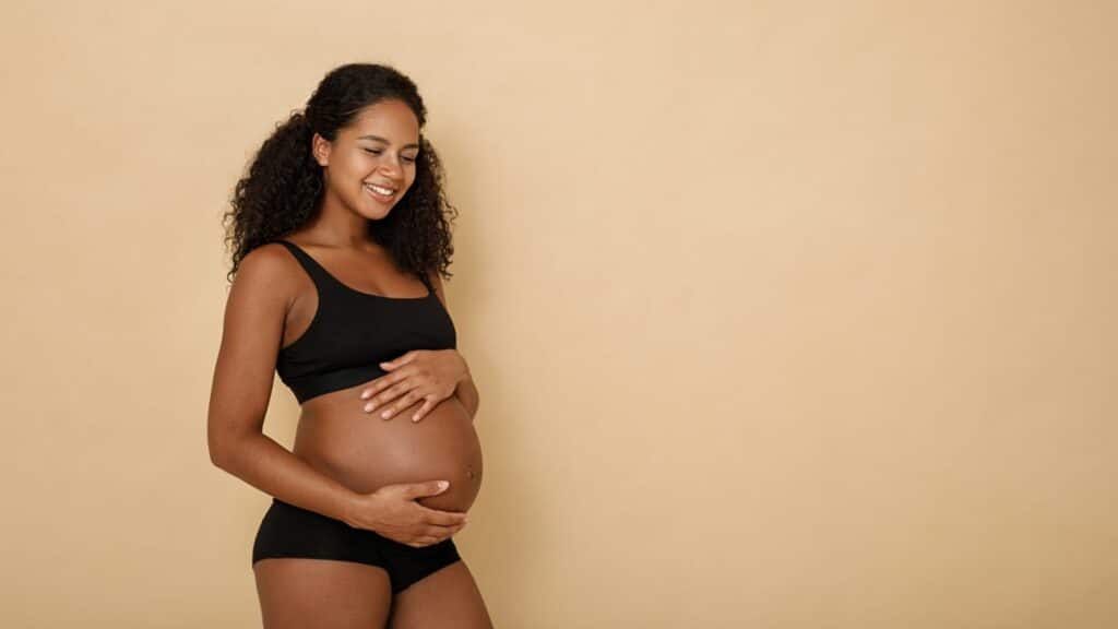 Imagem de uma mulher grávida sorrindo em um fundo bege