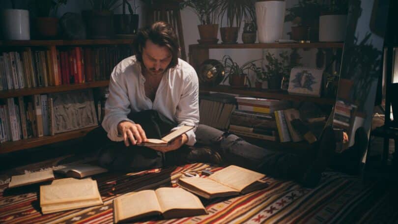 Imagem de um poeta lendo um livro e alguns outros a sua volta no chão
