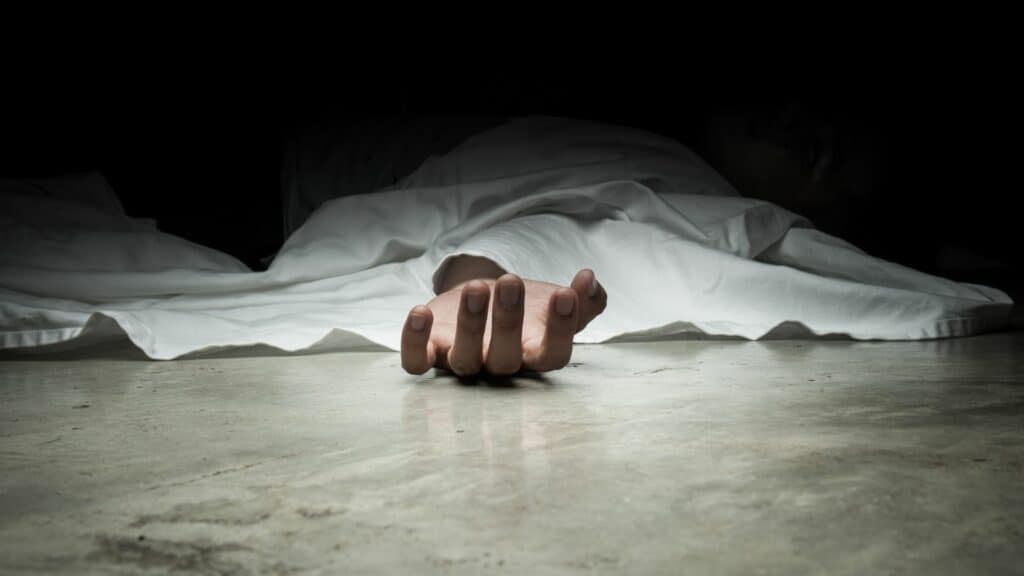 Imagem da mão de uma pessoa morta no chão coberta com um lençol branco