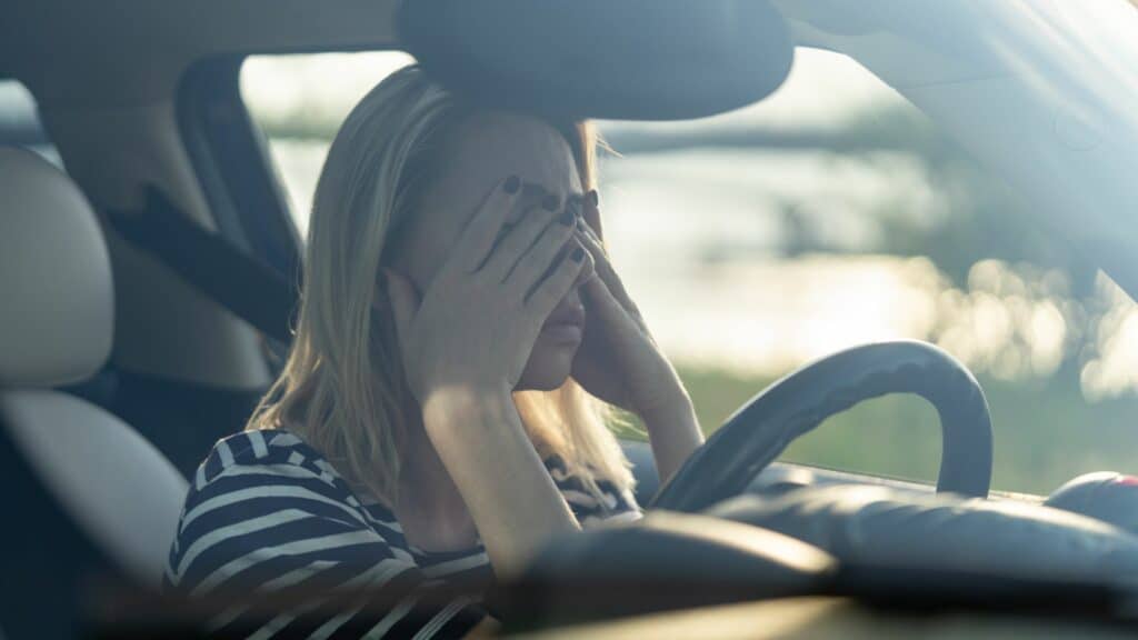 Imagem de uma mulher no carro com as mãos no rosto como se estivesse triste