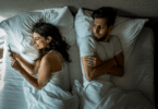 Casal deitado na cama enquanto homem olha para a mulher mexendo no celular