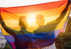Casal abraçado levantando a bandeira gay