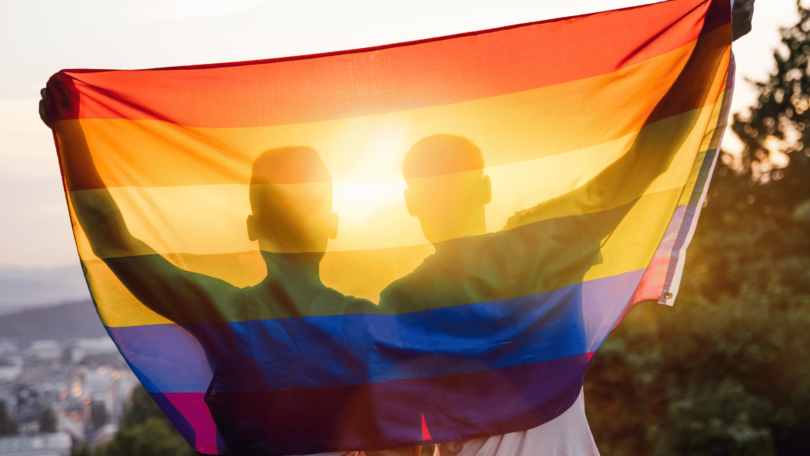 Casal abraçado levantando a bandeira gay