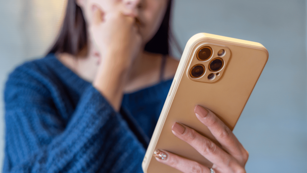 Mulher encarando o seu celular com a mão apoiada sobre o rosto e uma cara de dúvida.