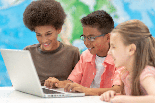 Três crianças mexendo em um computador e sorrindo