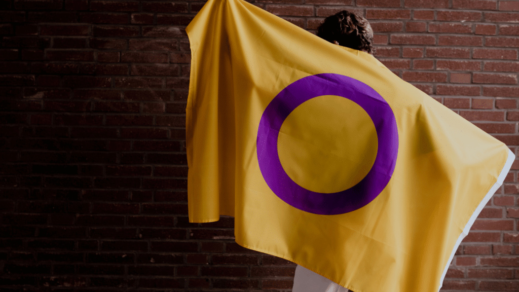 Pessoa segurando a bandeira intersexual, de cor amarela com círculo roxo. 