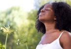 Mulher negra inspirando em um jardim, indicando estar sentindo paz.