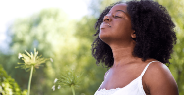 Mulher negra inspirando em um jardim, indicando estar sentindo paz.
