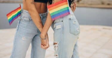 Duas mulheres segurando as mãos e a bandeira LGBTQIA+