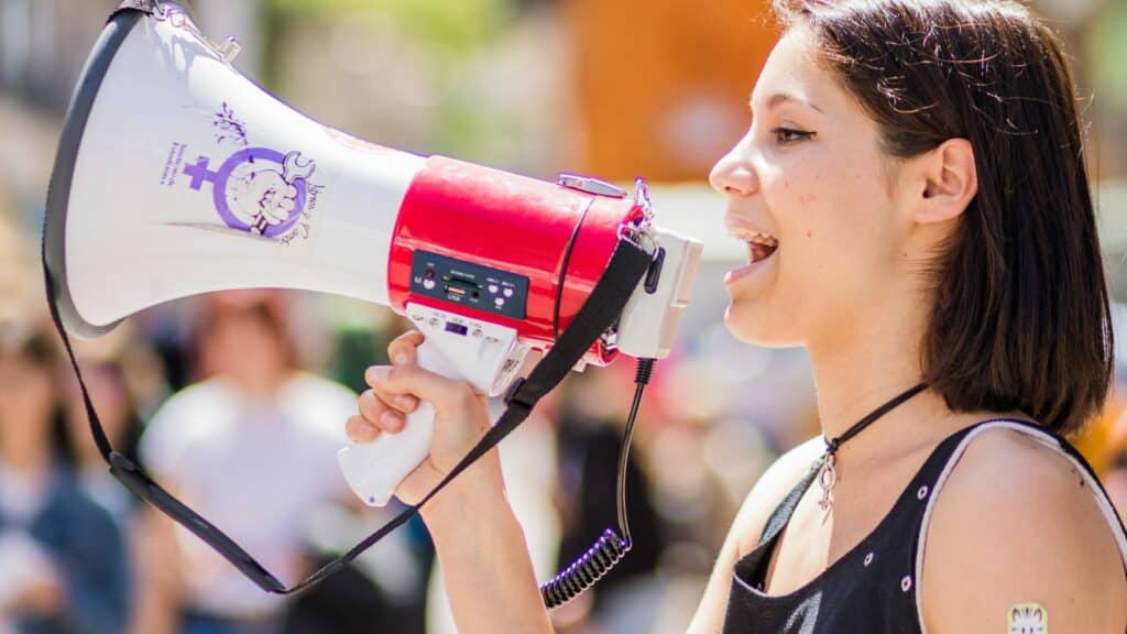 Imagem de uma mulher com um megafone na na mão, em meio a uma multidão, lutando pelos direitos feministas