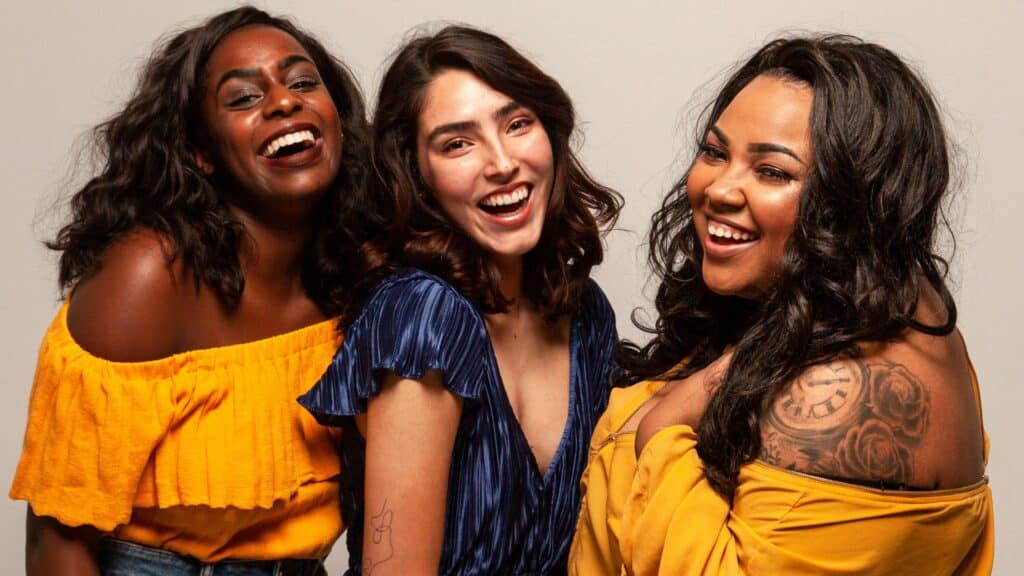 Imagem de três mulheres, uma negra, outra branca e a outra parda, sorrindo