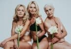 Imagem de três mulheres de meia idade, semi-nuas cada uma segurando uma flor branca.