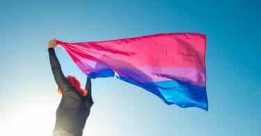 Imagem de uma moça segurando a bandeira da bissexualidade e o céu azul na paisagem