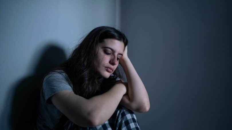 Imagem de uma mulher sentada no chão, chorando em um quarto em penumbra