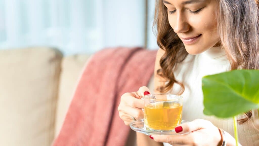 Imagem de uma mulher tomando chá com os olhos fechados e sorrindo