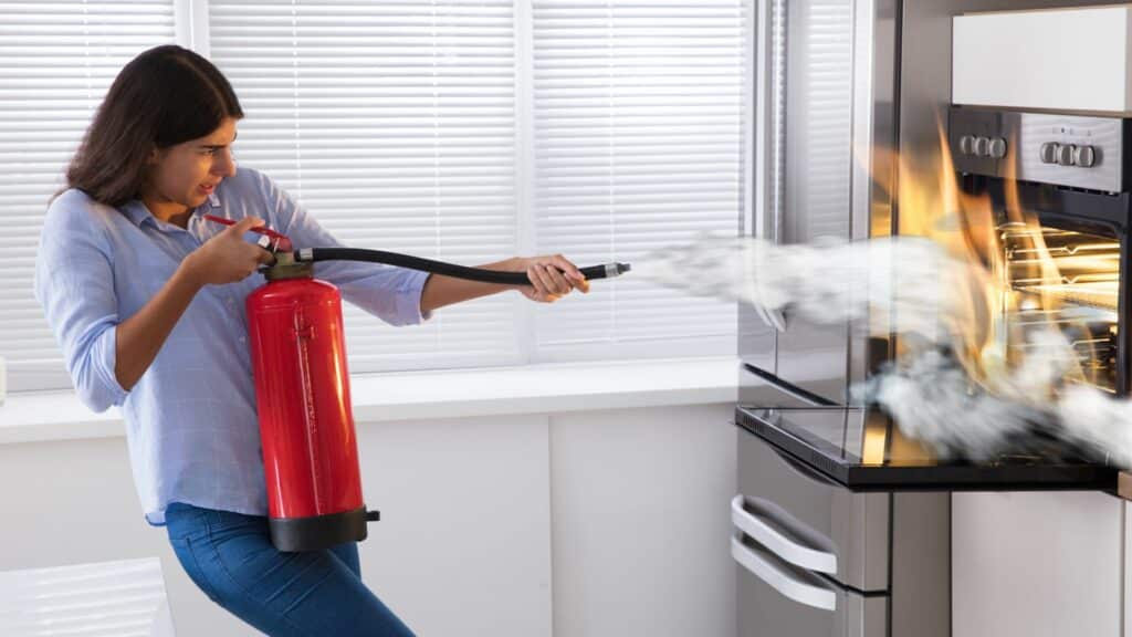 Imagem de uma mulher apagando fogo com extintor de incêndio em casa