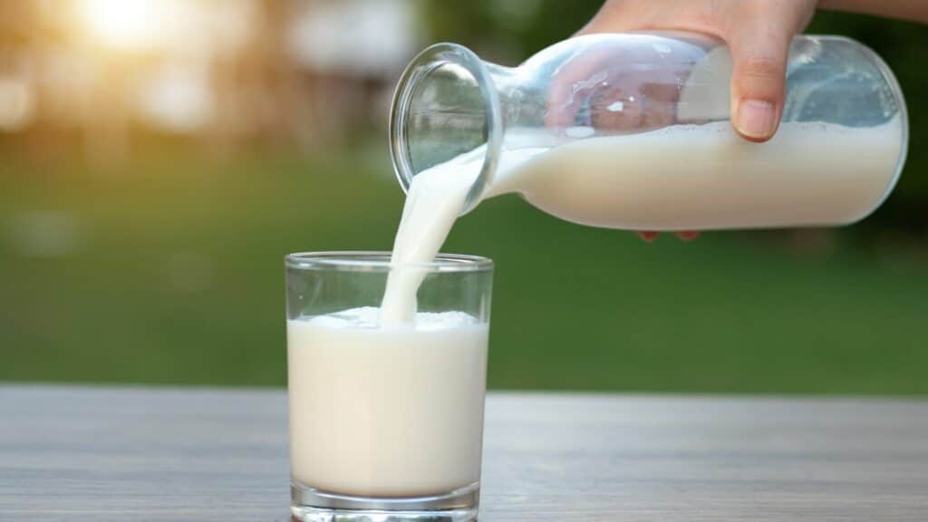 Imagem de uma pessoa colocando através de uma jarra o leite em um copo