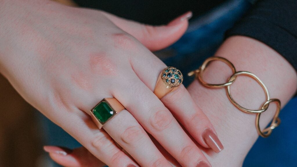 Imagem de mãos femininas usando anéis de esmeralda, um no dedo anelar e outro no indicador
