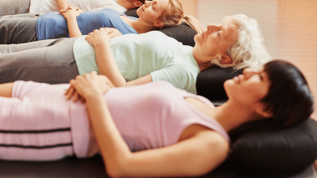 Grupo de mulheres deitadas, praticando exercício de respiração, durante uma sessão terapêutica.