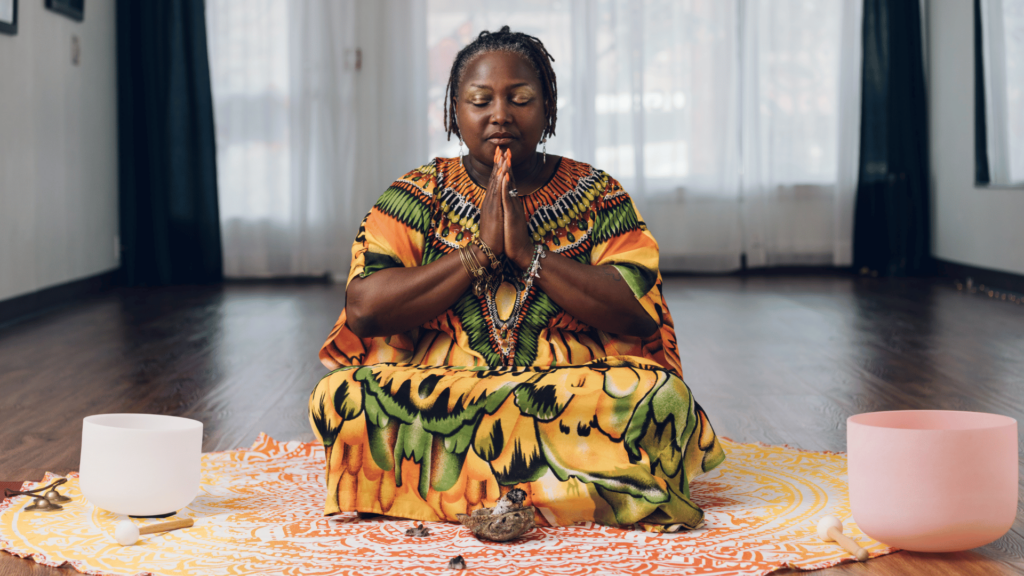 Mulher negra sentada com as pernas cruzadas em tapete enquanto medita. 