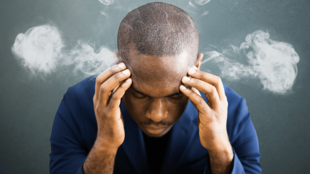 Homem negro estressado com as mãos sobre a testa.