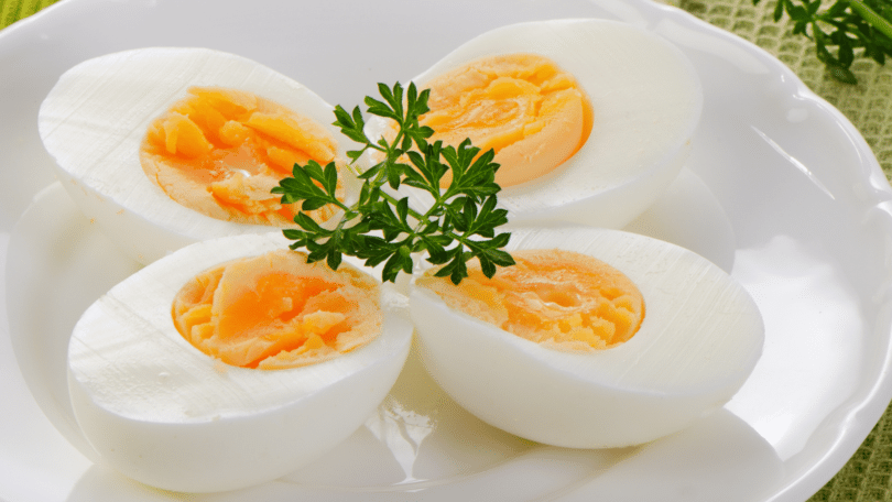 Imagem de quatros ovos cozidos em um prato com arranjo verde.