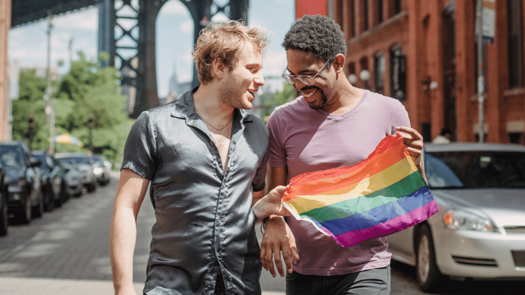 Casal de homens LGBTQIA+ segurando uma bandeira da comunidade gay. 