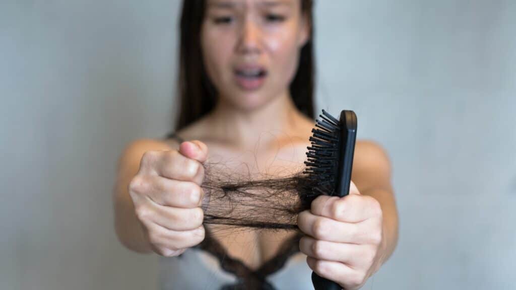 Imagem de uma mulher que está vendo seu cabelo cair no pente com feição de preocupação