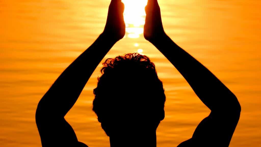 Imagem de um homem na frente do mar ao pôr-do-sol com as mãos erguidas