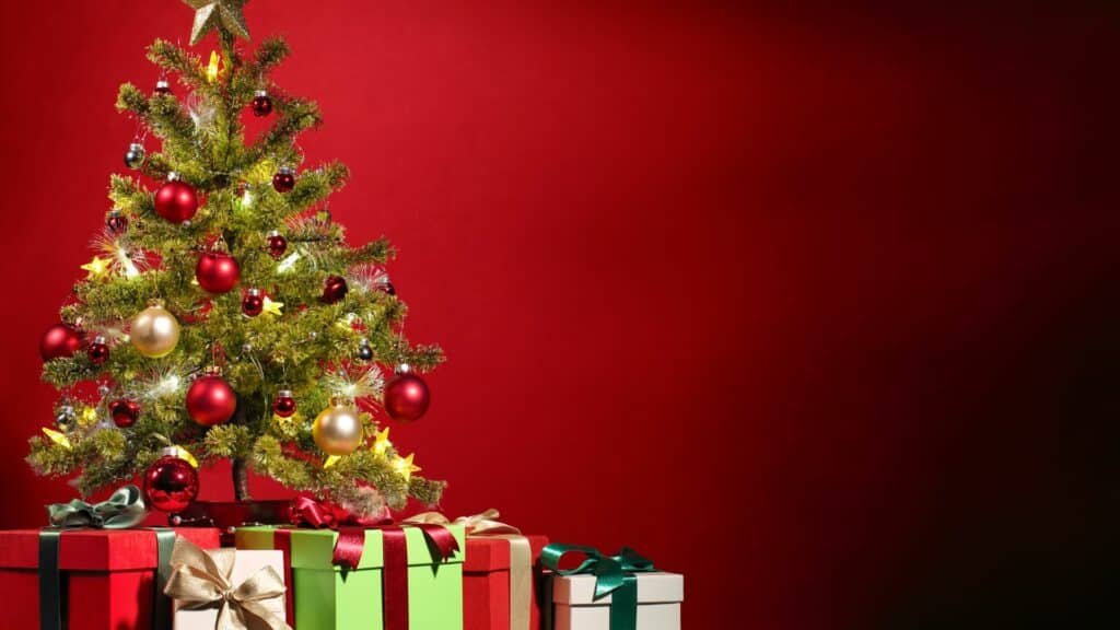 Imagem de uma árvore de Natal com uns presentes embaixo em um fundo vermelho
