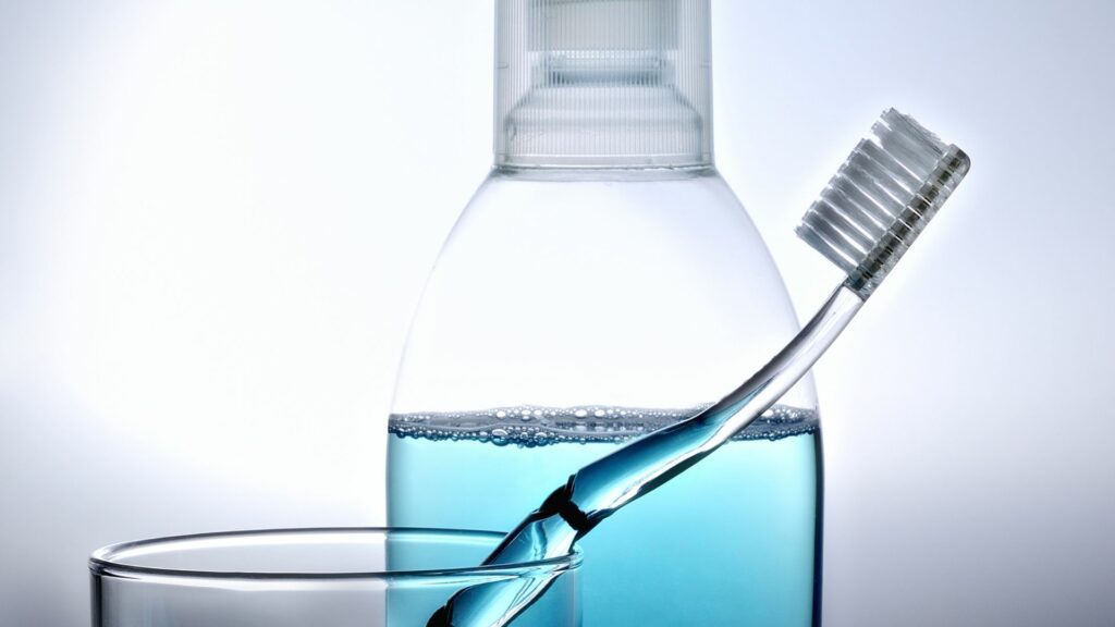 Imagem de uma escova de dente limpa em um copo, ao lado de um frasco de enxaguante bucal