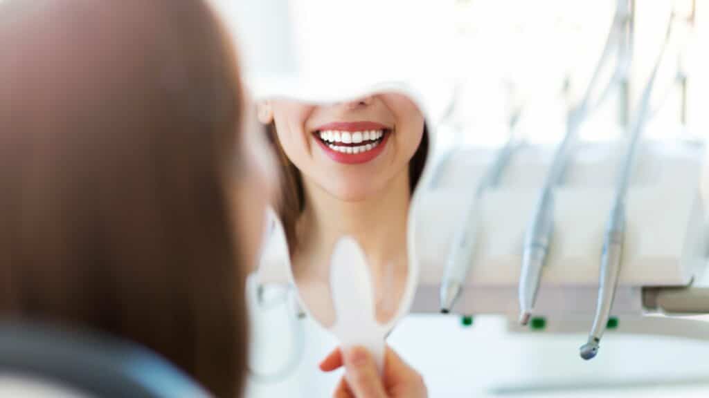 Imagem de uma mulher olhando os dentes em um espelho em formato de dente