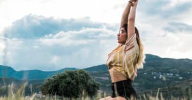 Imagem de uma mulher em um campo com os braços levantados como se estivesse meditando