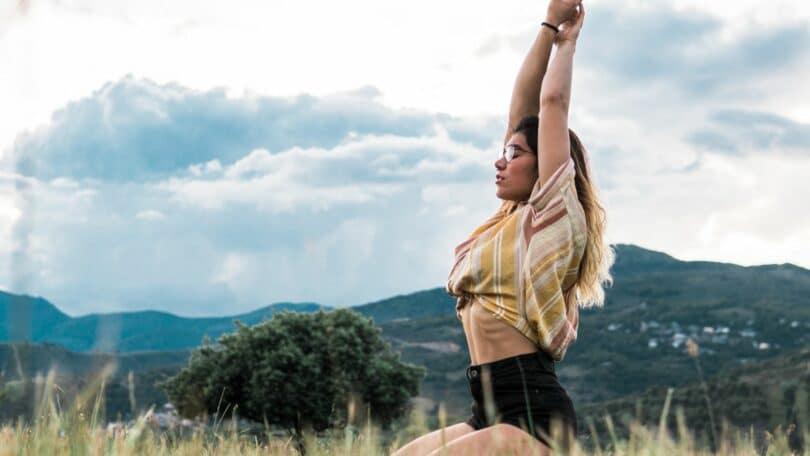 Imagem de uma mulher em um campo com os braços levantados como se estivesse meditando