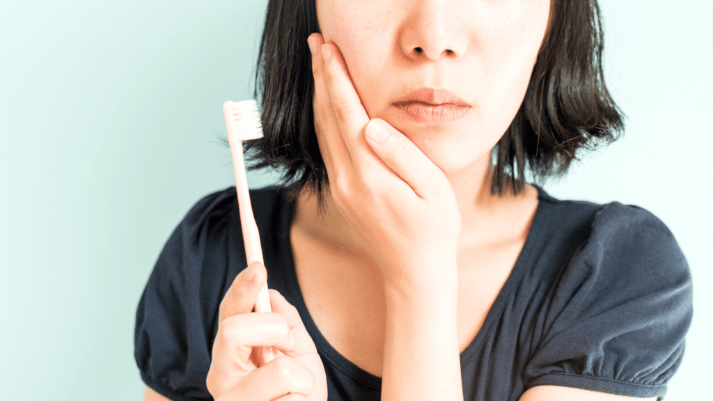 Mulher segurando escova de dentes com uma das mãos apoiadas no rosto