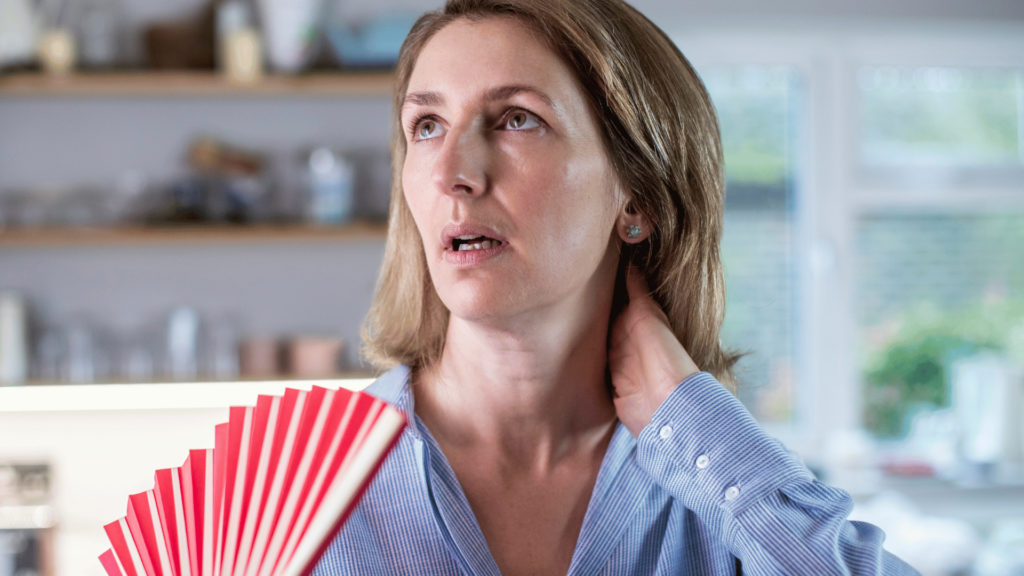 Mulher loira sofrendo com as ondas de calor da menopausa.