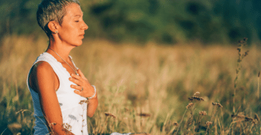 Mulher meditando no meio da natureza, com a mão sobre o peito. Representação de positividade e resiliência.