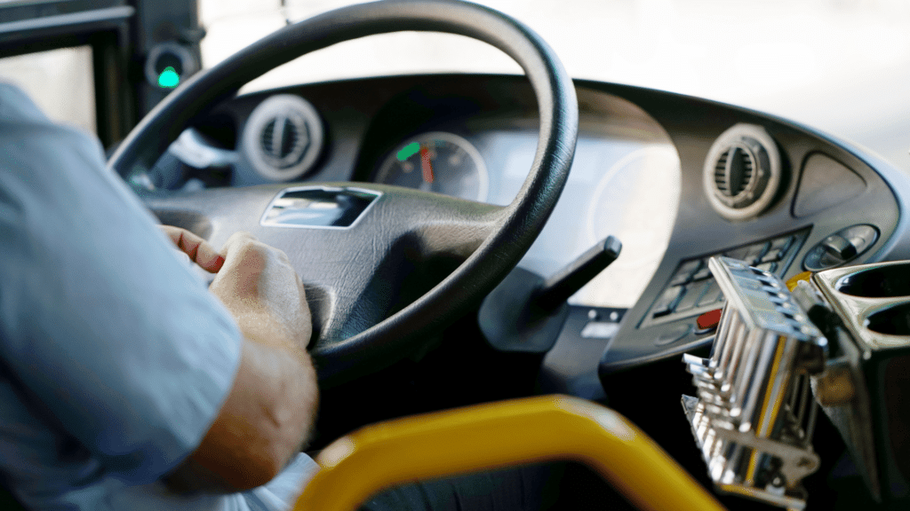 Visão do volante do motorista de um ônibus. Ele está sentado na frente do volante. 