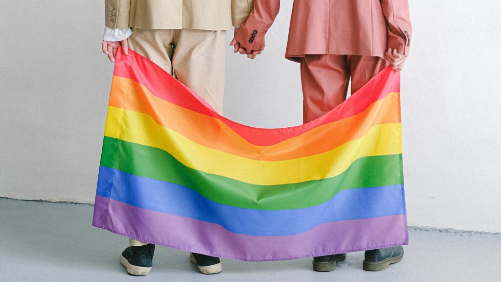 Casal homossexual de costas segurando uma bandeira LGBTQIA+