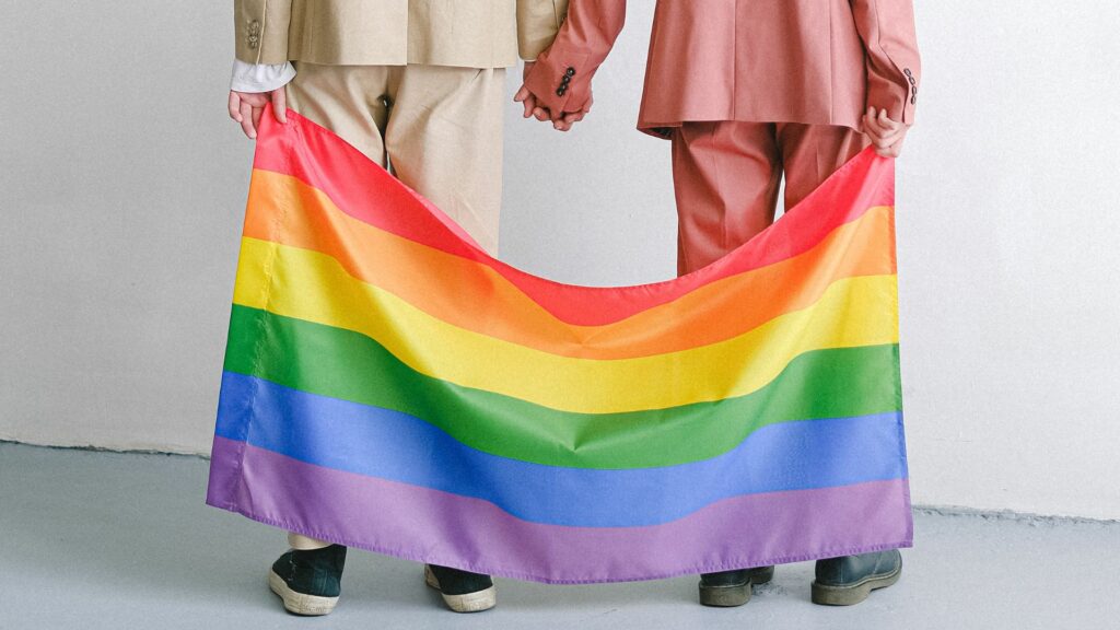Casal homossexual de costas segurando uma bandeira LGBTQIA+