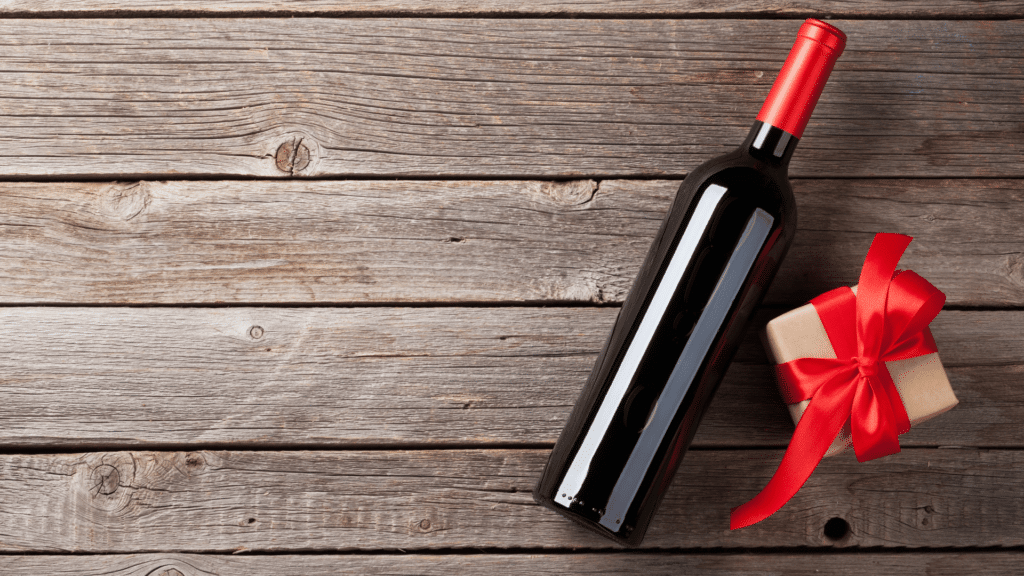 Garrafa de vinho com pequena caixa de presente ao lado, com um laço vermelho. 