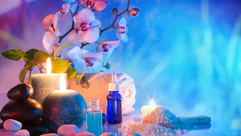 Imagem de uma mesa com velas, flores, aromas e pedras em uma sala com luz azul