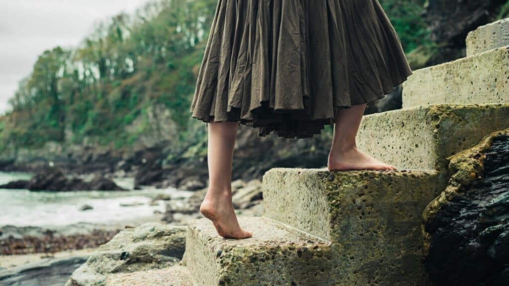 Imagem de uma mulher descalça subindo escadas à beira de um riacho