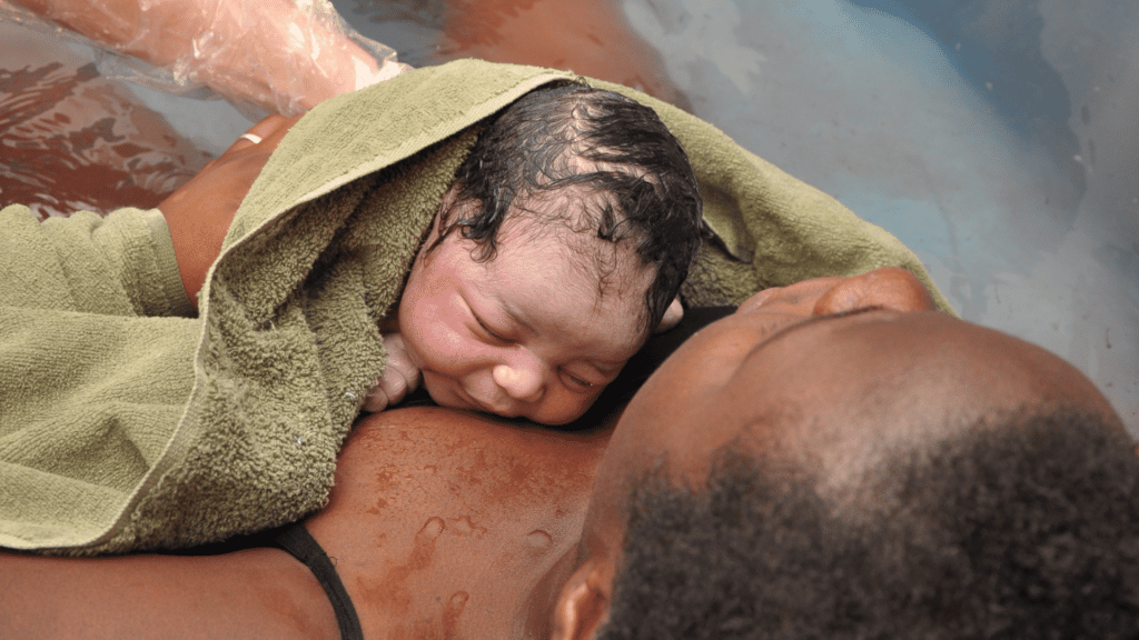 Mulher com seu bebê no colo após ter parto na água. 