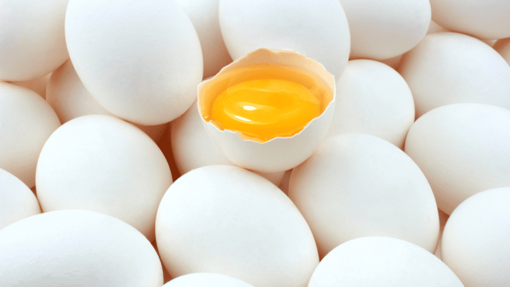 Ovos brancos. Um dos ovos está aberto e é possível ver a gema amarela. 