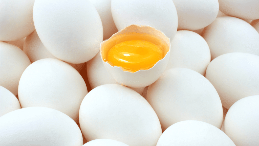 Ovos brancos. Um dos ovos está aberto e é possível ver a gema amarela.