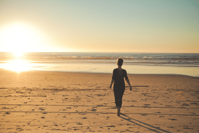 Mulher andando no meio da praia, refletindo sobre a vida